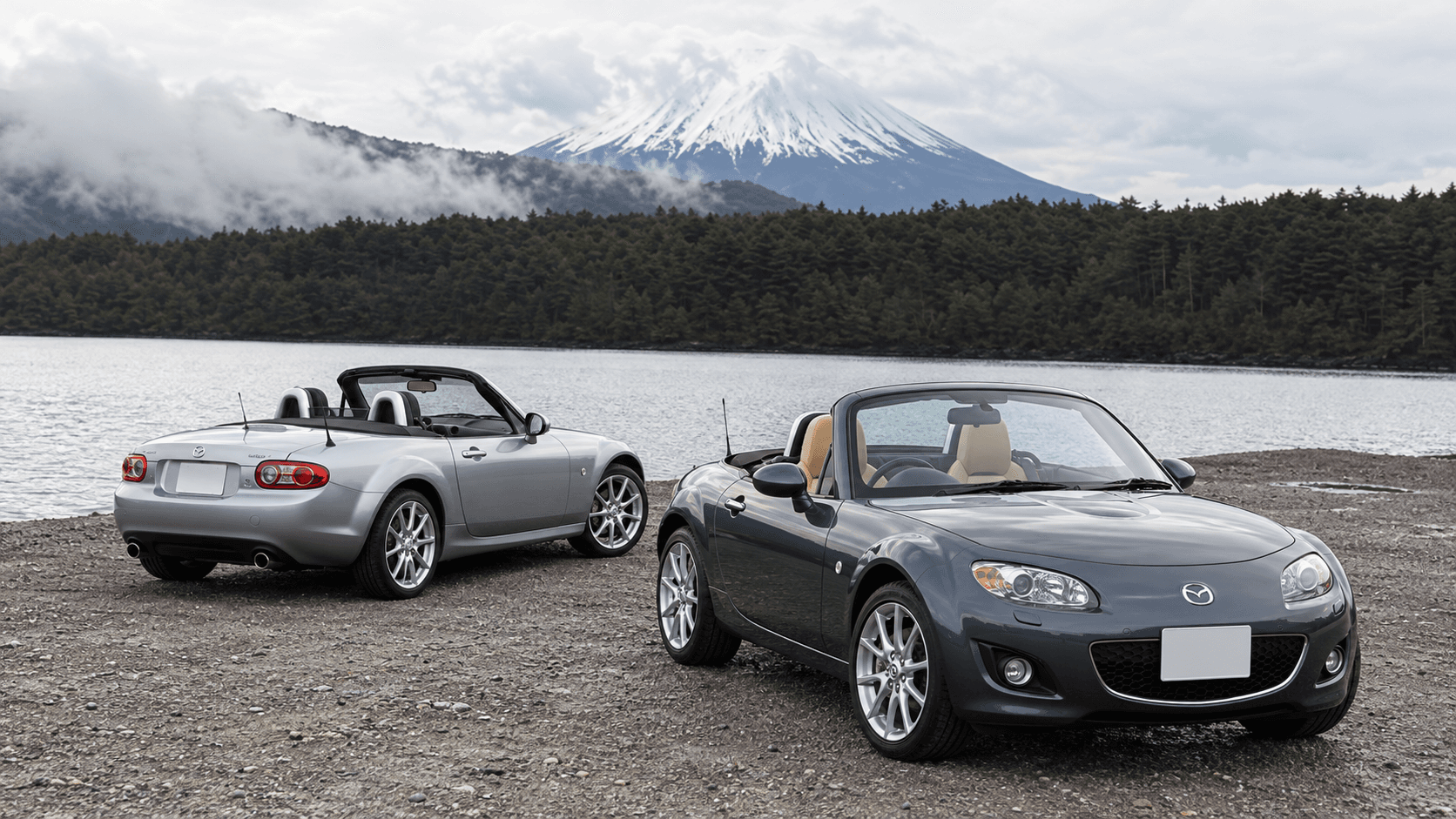 Silver and dark grey Mazda Roadster / MX-5 cars beside a lake with Mt. Fuji in the background
